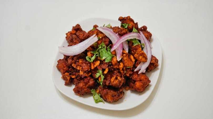 Chicken 65, a South Indian fried chicken dish, garnished with red onions and cilantro on a white plate.