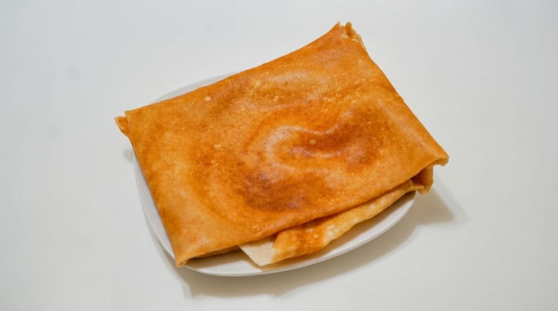Golden brown dosa, a thin Indian pancake, folded on a white plate against a white background.